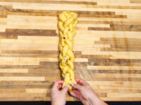 Hands shaping a braided Christmas Vánočka (Houska) dough with raisins on a wooden board.