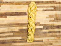Braided Christmas Vánočka (Houska) dough with raisins, unbaked, on a wooden board.