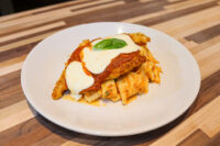Chicken Parmesan Chicken Parmesan topped with marinara sauce, melted mozzarella, and a basil leaf, served over tube-shaped pasta on a white plate.