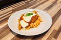 Chicken Parmesan Chicken Parmesan cutlet with marinara and melted mozzarella over rigatoni, basil garnish, white plate.