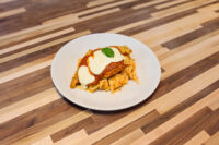 Chicken Parmesan Chicken Parmesan cutlet topped with marinara sauce, melted cheese, and basil, served over pasta on a white plate.
