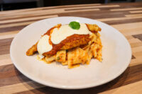 Chicken Parmesan Chicken Parmesan cutlet topped with tomato sauce, melted cheese, and a basil leaf, served over pasta on a white plate.