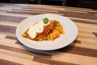 Chicken Parmesan Chicken Parmesan topped with marinara and melted cheese, basil garnish, served with pasta on a white plate.