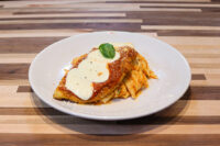 Chicken Parmesan Breaded Chicken Parmesan topped with tomato sauce, melted cheese, and basil on a white plate.