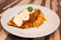 Chicken Parmesan Breaded Chicken Parmesan topped with marinara, melted cheese, and basil, served over ribbon pasta on a white plate
