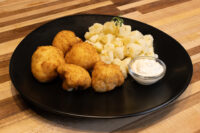 Fried Cauliflower Smažený Květák bites on a black plate with diced potatoes and white dip.