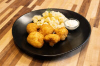 Golden breaded Fried Cauliflower Smažený Květák pieces with diced potatoes and a dip on a black plate.