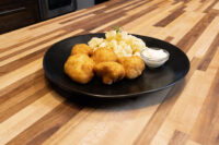 Golden fried Cauliflower Smažený Květák bites with potato salad and a creamy dip on a black plate.