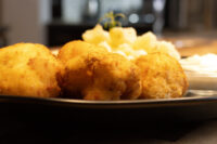 Golden breaded Fried Cauliflower Smažený Květák pieces on a dark plate with mashed potato and a herb sprig