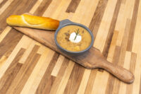Bowl of Valašská Kyselica Soup with sour cream and rosemary, served with a baguette on a wooden board