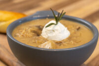 Bowl of Valašská Kyselica Soup with visible vegetable chunks, sour cream dollop, and rosemary sprig