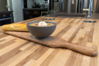 Bowl of creamy Valašská Kyselica Soup topped with sour cream and rosemary, served with bread on a wooden board.