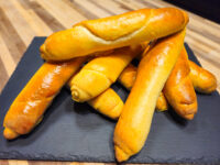 Czech Rolls Rohliky Recipe Stack of glossy golden Czech Rolls Rohliky, tapered and baked, piled on a dark slate board.