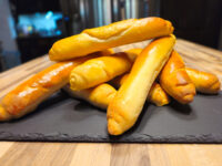 Czech Rolls Rohliky Recipe Golden-brown Czech Rolls Rohliky, elongated and tapered, piled on a dark slate board on wood.