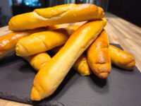 Czech Rolls Rohliky Recipe Stacked golden-brown Czech Rolls Rohliky piled on a dark slate board.