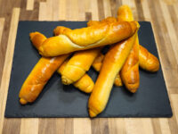 Czech Rolls Rohliky Recipe Pile of glossy golden Czech Rolls Rohliky, shaped into long tapered sticks, on a dark slate board.