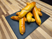 Czech Rolls Rohliky Recipe Pile of glossy, twisted Czech Rolls Rohliky on a dark slate board atop a wooden table.