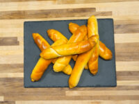 Czech Rolls Rohliky Recipe Golden-brown Czech Rolls Rohliky piled on a dark slate board on a wooden table.