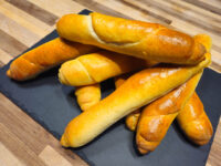 Czech Rolls Rohliky Recipe A pile of golden-brown Czech Rolls Rohliky with scored tops, stacked on a dark slate board.