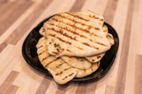 Stack of grilled naan bread with char marks piled on a black plate on a wooden table.