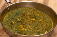 Spinach Palak Paneer Stainless steel pan of Spinach Palak Paneer with pale paneer chunks in thick green curry.