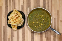 Spinach Palak Paneer Pan of green Spinach Palak Paneer curry beside grilled flatbread wedges on a black plate.
