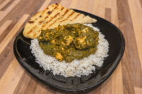 Spinach Palak Paneer Spinach Palak Paneer with cubed paneer over rice, served with grilled flatbread on a black plate.