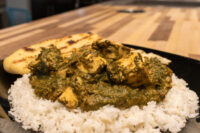 Spinach Palak Paneer Spinach Palak Paneer with cubed paneer over rice, grilled flatbread on a black plate