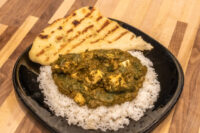 Spinach Palak Paneer Spinach Palak Paneer with cubed paneer over rice, served with grilled flatbread on a black plate.