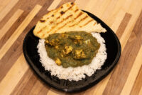 Spinach Palak Paneer Spinach Palak Paneer curry with cubed paneer over rice, served with grilled naan on a black plate.