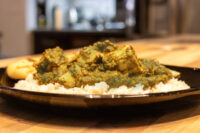 Spinach Palak Paneer Spinach Palak Paneer with cubed paneer over rice on a black plate, flatbread at the edge.