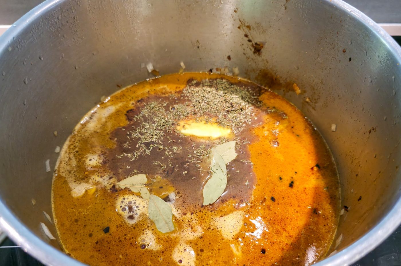 Pot of orange chicken broth simmering with bay leaves, thyme, and melting butter for Kuře na Paprice.
