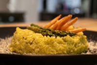 Asparagus Risotto with Shrimp Yellow Asparagus Risotto with Shrimp topped with grilled asparagus spears and curled shrimp on a dark plate.