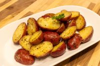 Baby Red Potatoes with Butter Halved Baby Red Potatoes with Butter, skins and gold flesh showing, on a white oval plate