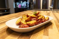 Baby Red Potatoes with Butter Baby Red Potatoes with Butter, quartered and glazed with a buttery sheen, served in a white oval dish on a wooden counter with a kitchen blurred behind it.