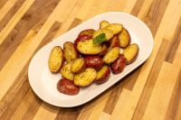 Baby Red Potatoes with Butter Halved Baby Red Potatoes with Butter, golden and glossy, garnished with parsley on a white oval plate.