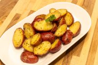 Baby Red Potatoes with Butter Halved Baby Red Potatoes with Butter, golden and glossy, on a white oval platter with parsley.