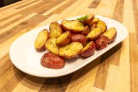 Baby Red Potatoes with Butter Halved red potatoes glazed in butter with pepper flecks, plated on a white oval dish on a wooden table.