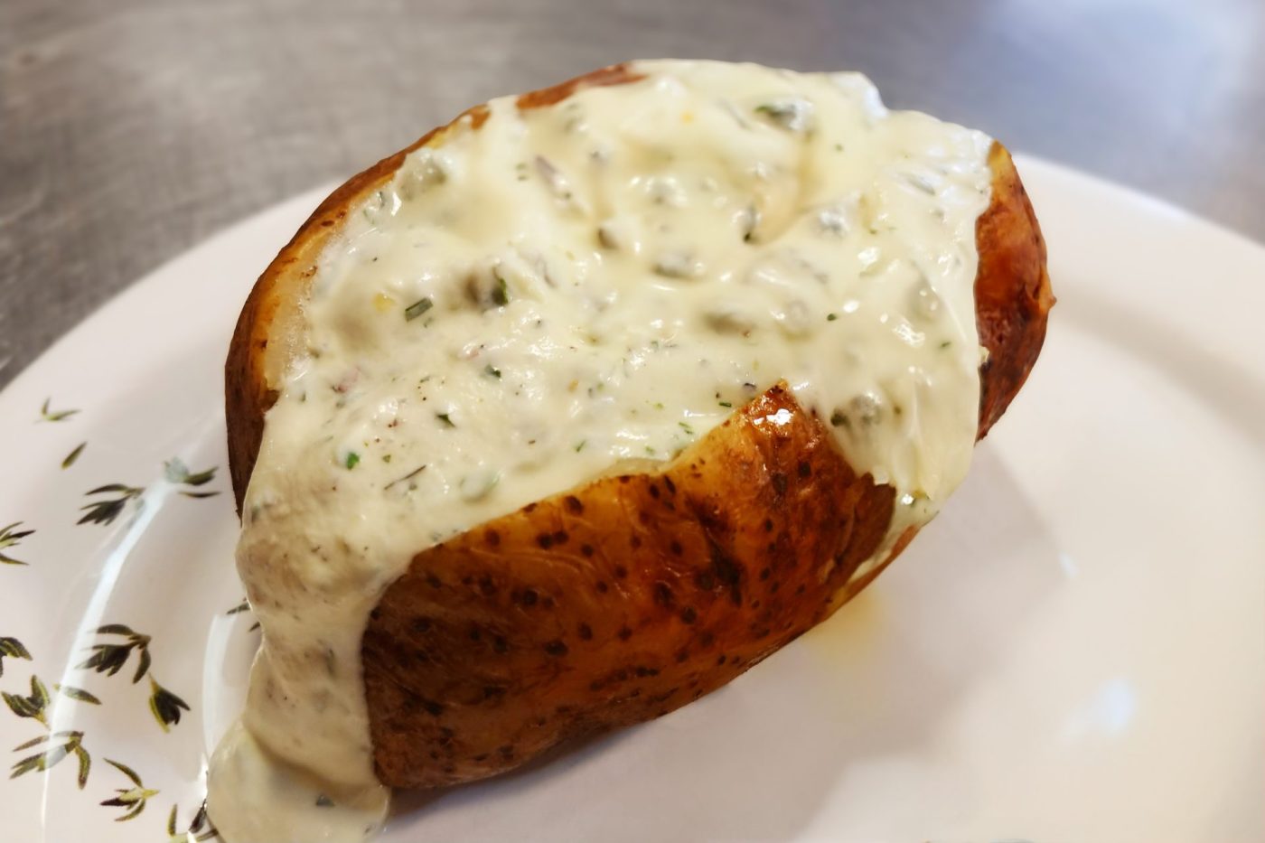 Split baked potato topped with a generous scoop of herbed sour cream on a white plate