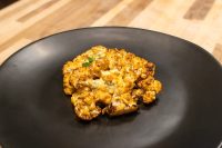 Roasted Buffalo Cauliflower Steak topped with melted blue cheese and herb garnish on a dark plate.