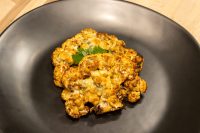 Roasted Buffalo Cauliflower Steak florets with melted cheese and parsley garnish on a black plate