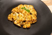 Roasted Buffalo Cauliflower Steak with melted cheese and charred edges, garnished with parsley on a black plate