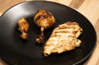 Grilled Lemon and Garlic Chicken drumstick and breast with char marks on a black plate