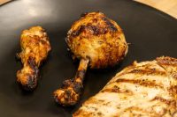 Grilled Lemon and Garlic Chicken drumsticks and breast piece with char marks on a black plate