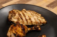 Grilled Lemon and Garlic Chicken breast with char marks beside a drumstick on a black plate.