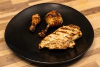 Grilled Lemon and Garlic Chicken drumsticks and breast with char marks on a black plate.