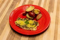 Pesto Chicken Breasts Pesto Chicken Breasts topped with herbed cheese, plated with roasted potato halves on a red dish.