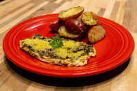 Pesto Chicken Breasts Pesto Chicken Breasts topped with green herb coating and parmesan, served with roasted potato halves on a red plate