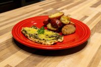 Pesto Chicken Breasts Pesto Chicken Breasts with green herb coating, parsley garnish, and roasted red potatoes on a red plate