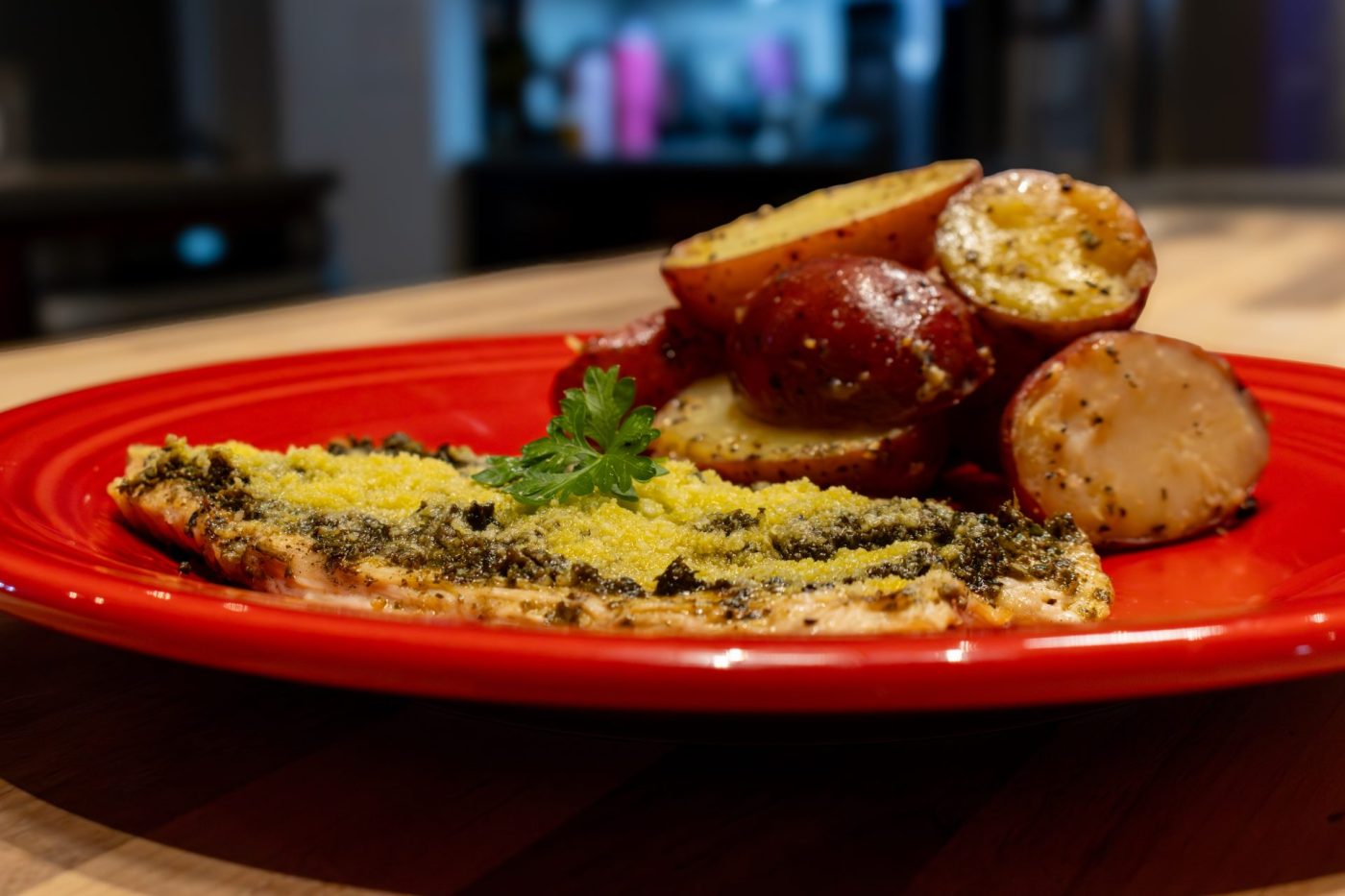 Pesto Chicken Breasts Pesto Chicken Breasts with a green herb-and-cheese crust on a red plate, parsley garnish, roasted potatoes beside it.